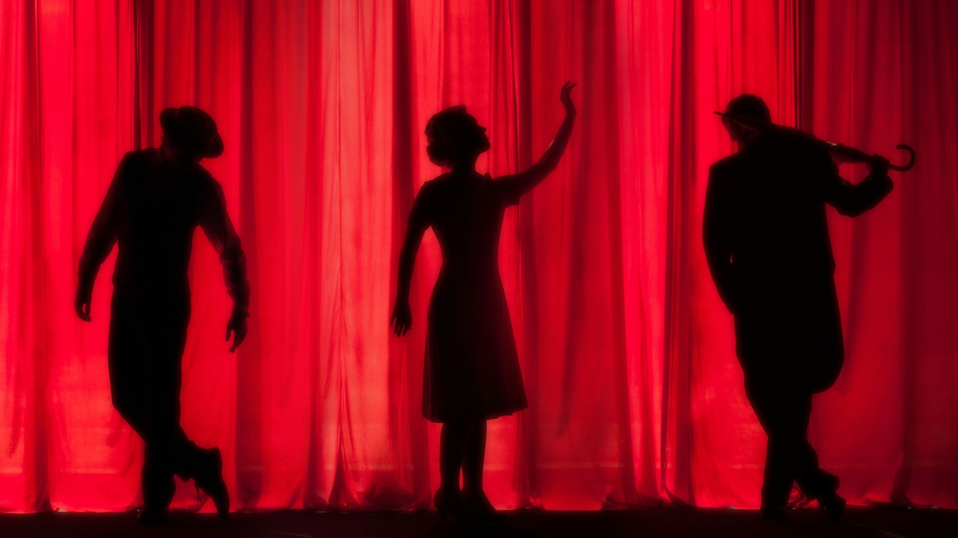 Characters on stage behind a red theatre curtain